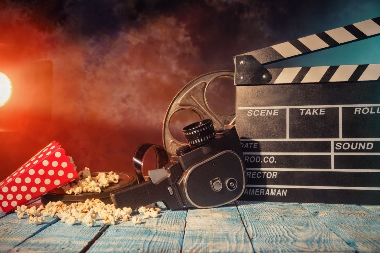 A movie clapper, popcorn, and a film reel on a wooden table.